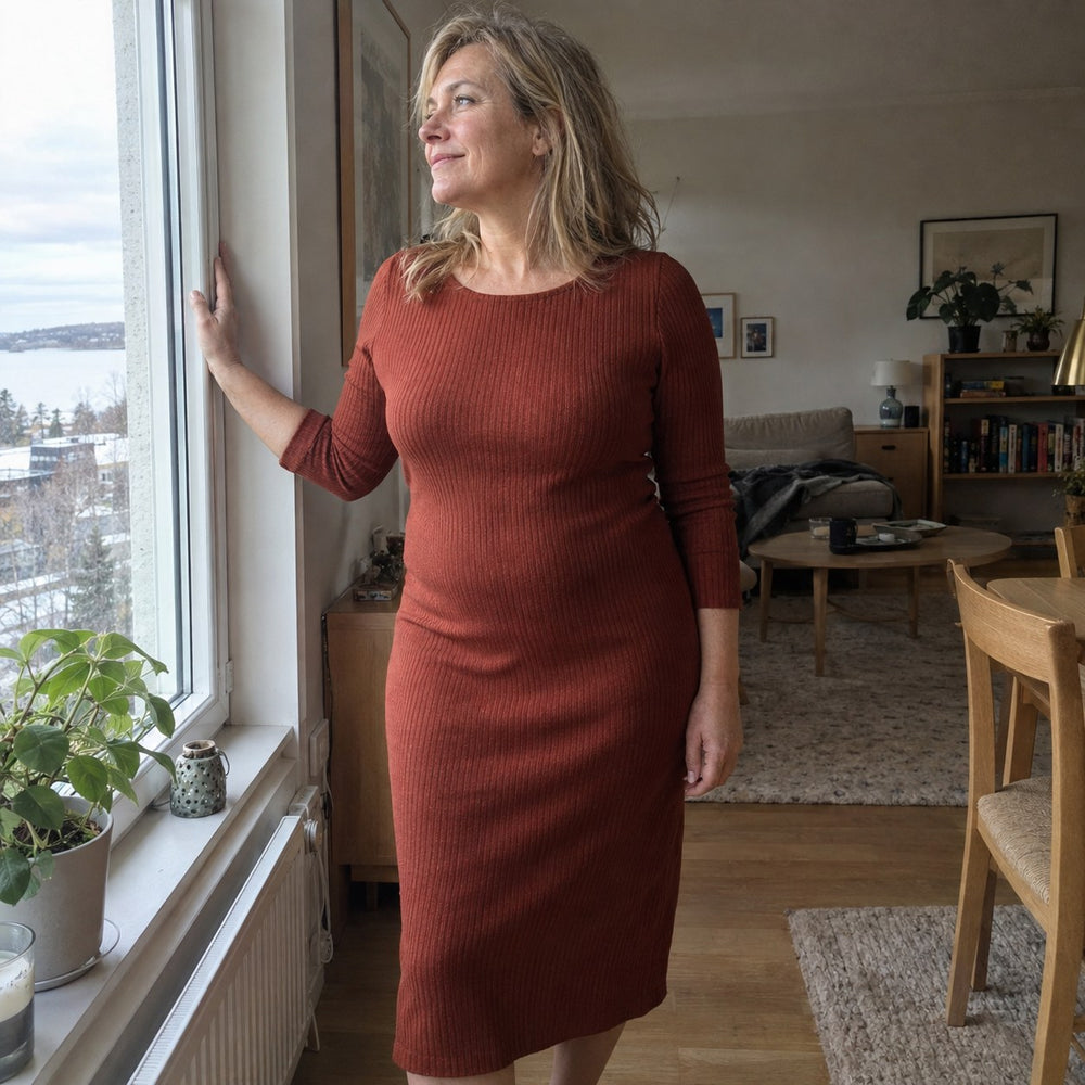Kvinna i åtsittande klänning vid fönstret hemma